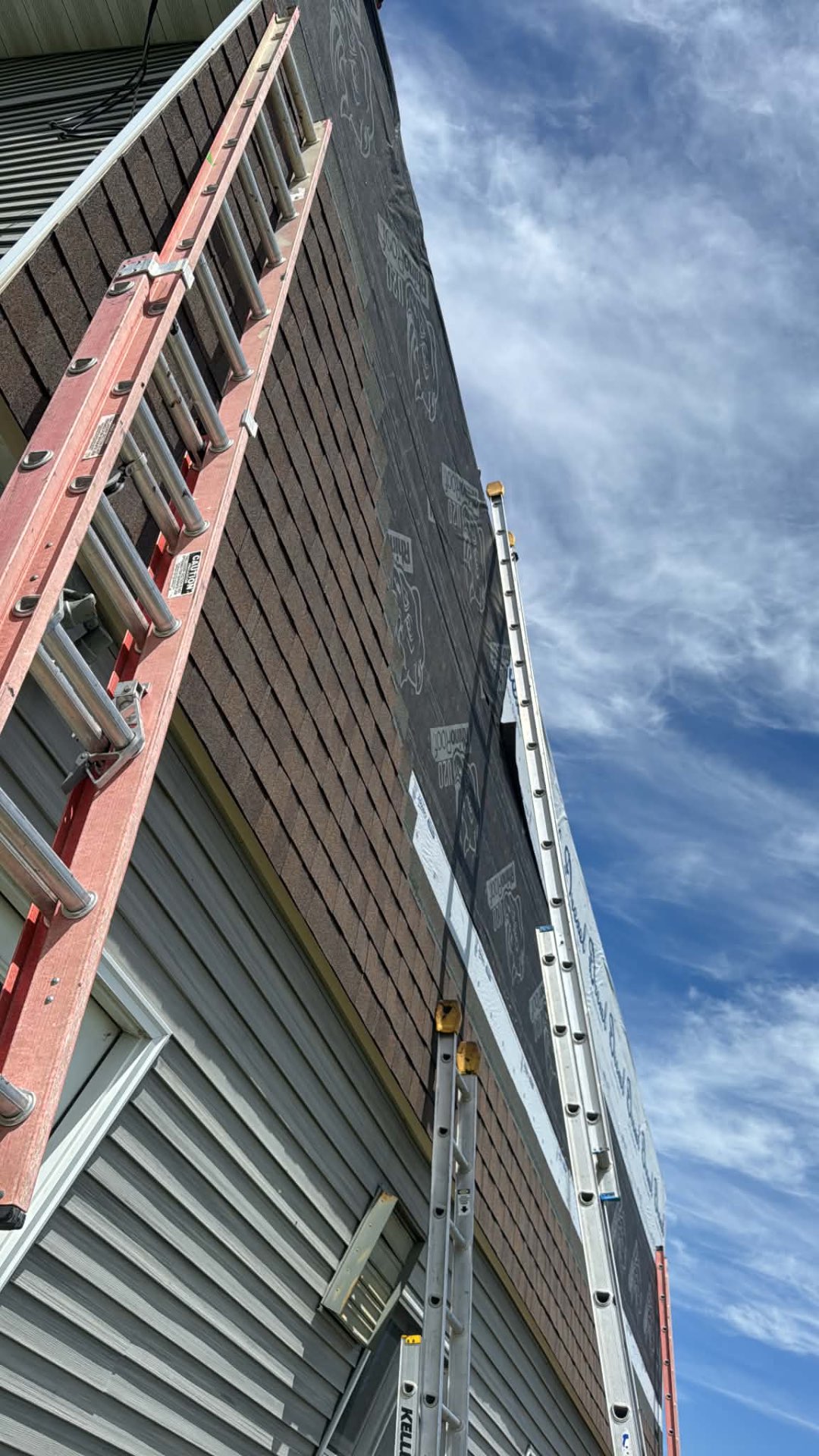 Ladders set against a tall steep shingled wall section during roofing work