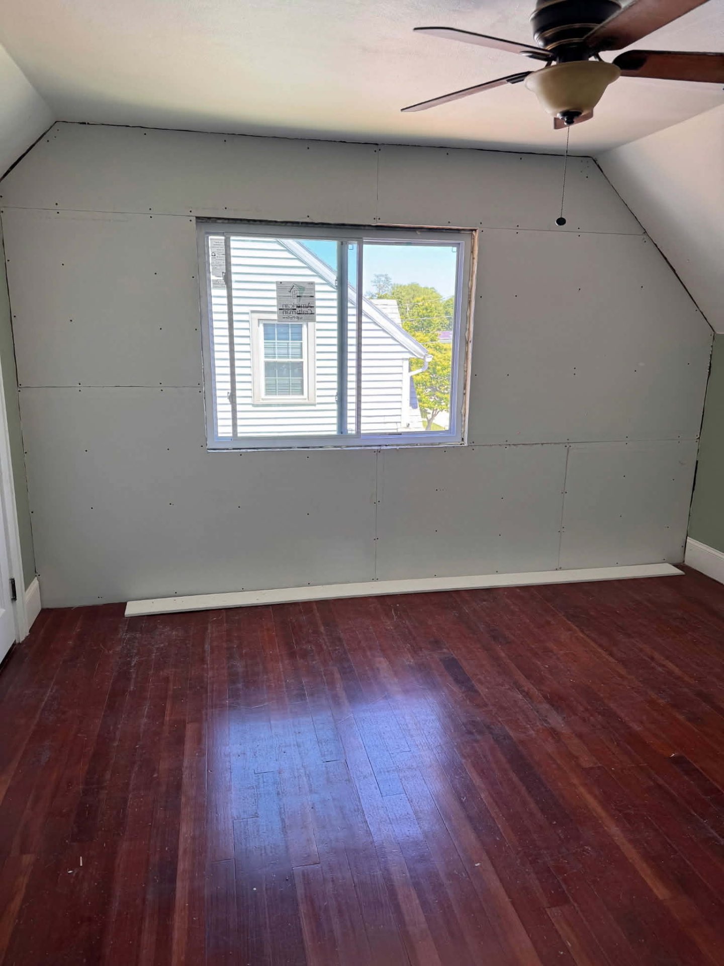 Sloped-ceiling bedroom with new drywall board hung around the window