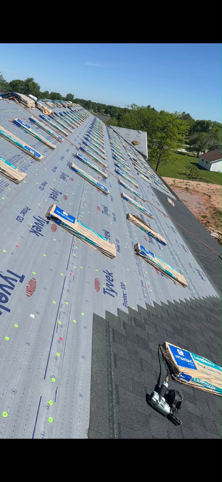 Shingle bundles staged in rows across a wrapped roof deck mid-install