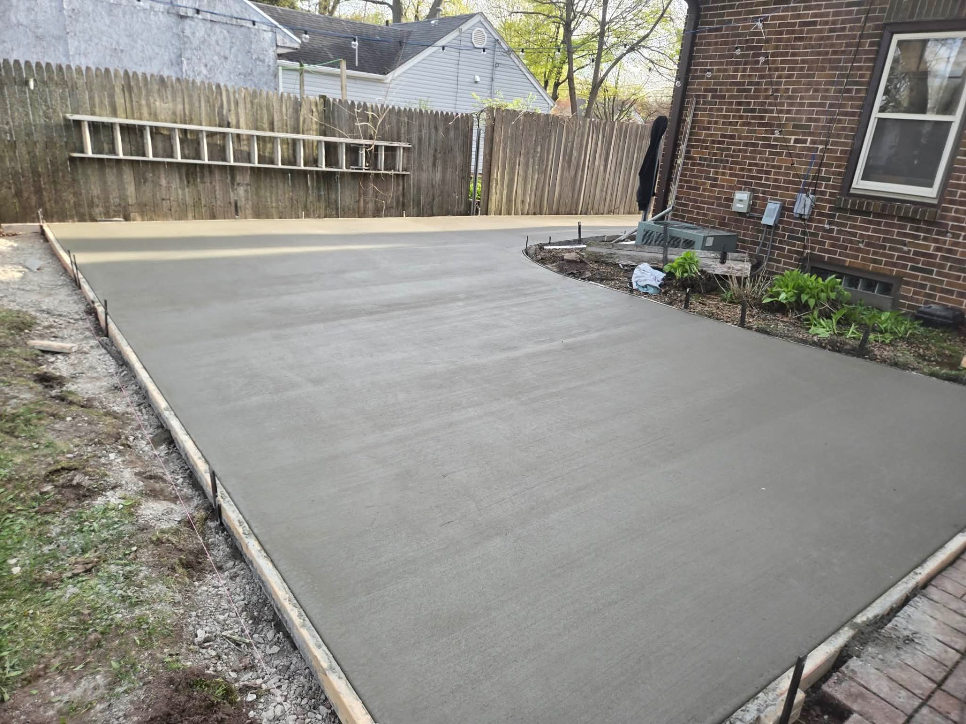 Large finished backyard concrete patio poured to grade beside a brick home